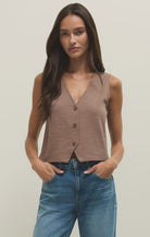 Woman wearing a brown sleeveless top and blue jeans against a plain background