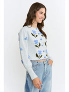 The Amelie Floral Cardigan in light grey with delicate blue floral embroidery and green stem details.
