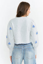 The Amelie Floral Cardigan in light grey with delicate blue floral embroidery and green stem details.
