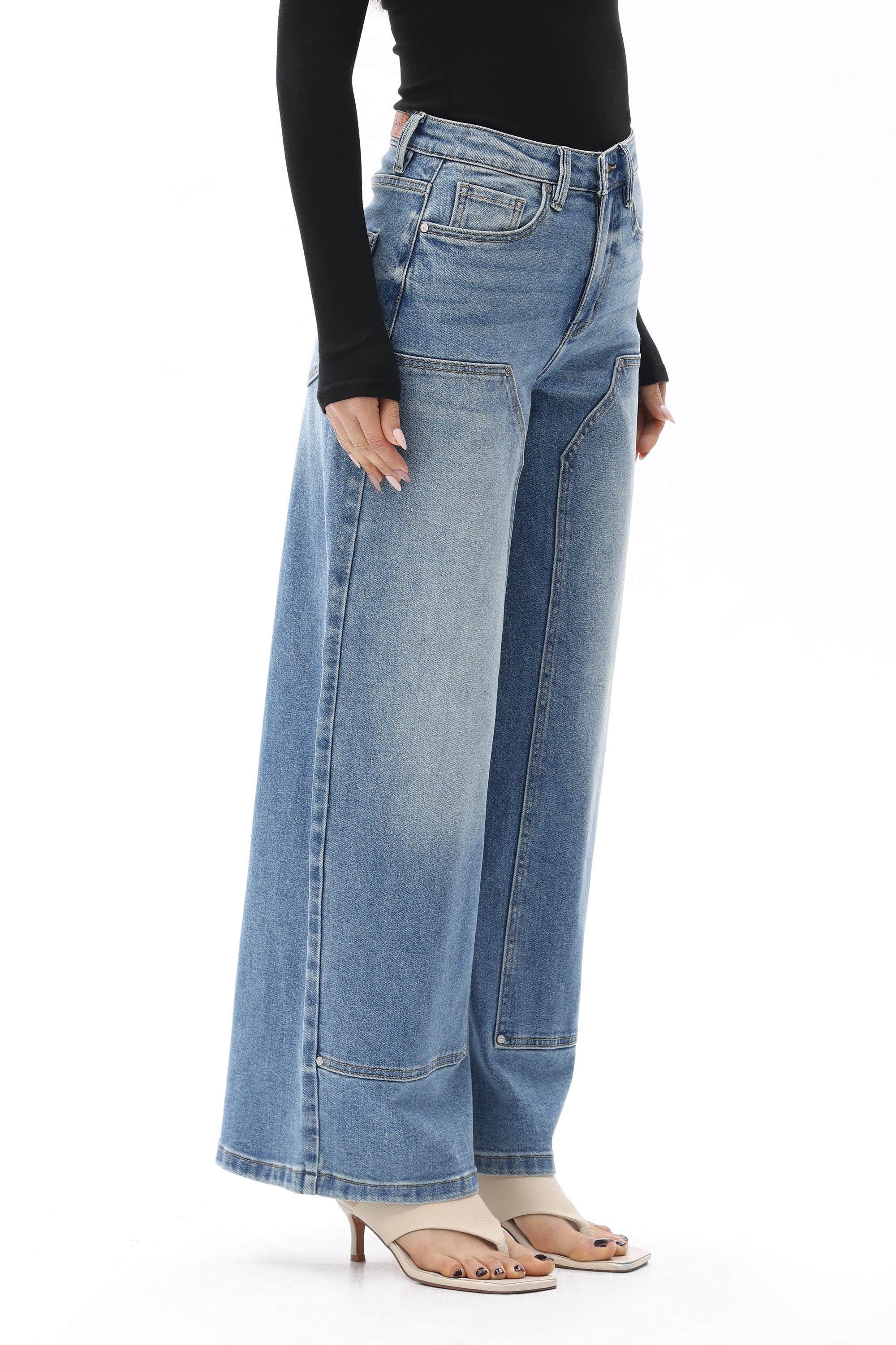 Model wearing BAYEAS Valentine High Rise Barrel Jeans in a medium blue wash, featuring a high-rise waist, relaxed barrel-leg silhouette, subtle fading, front panel seam detailing, classic five-pocket styling, and a full-length fit. Styled with a black long-sleeve top and nude thong sandals.
