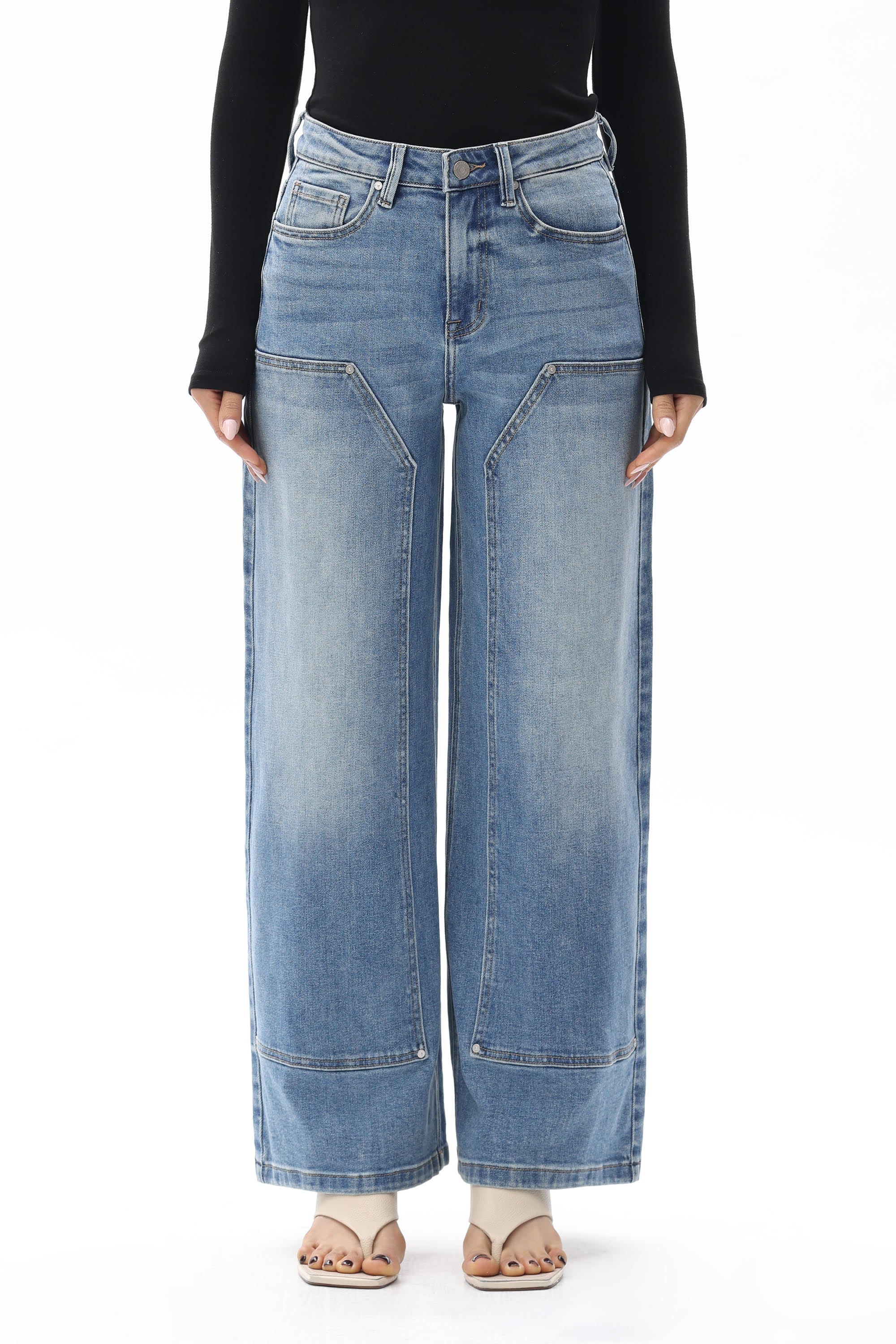 Model wearing BAYEAS Valentine High Rise Barrel Jeans in a medium blue wash, featuring a high-rise waist, relaxed barrel-leg silhouette, subtle fading, front panel seam detailing, classic five-pocket styling, and a full-length fit. Styled with a black long-sleeve top and nude thong sandals.

