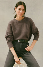 Woman wearing a grey-brown sweater and black pants against a neutral background