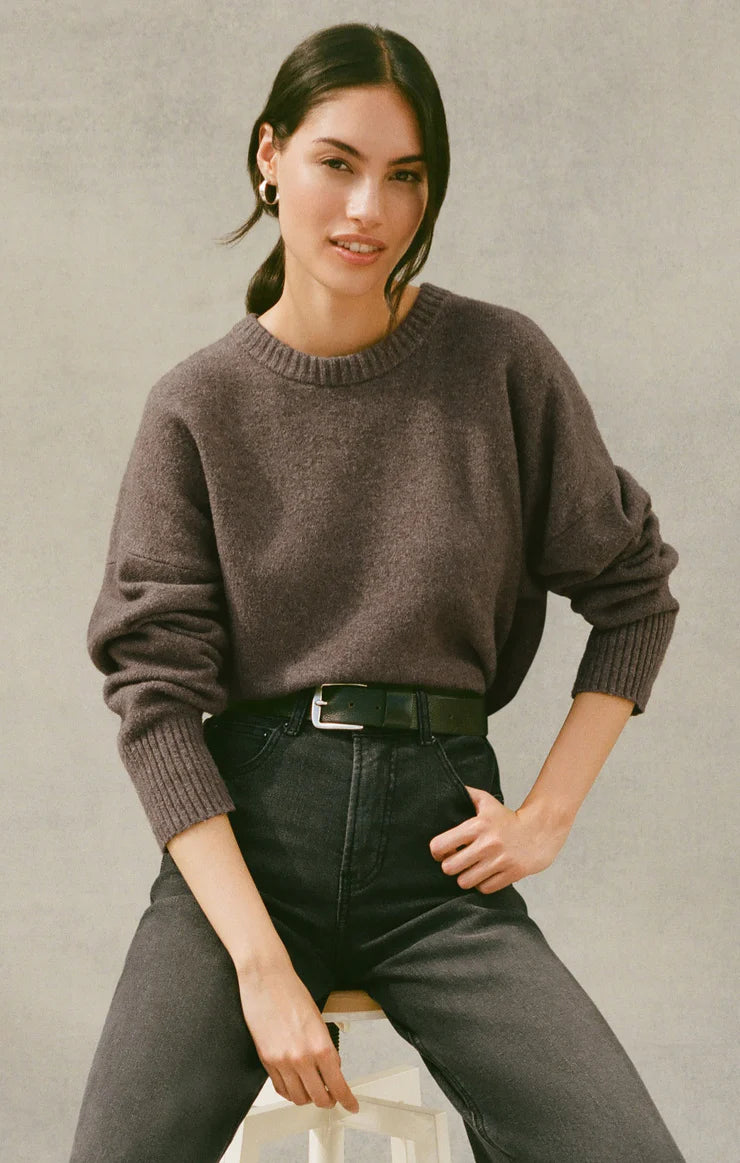 Woman wearing a grey-brown sweater and black pants against a neutral background