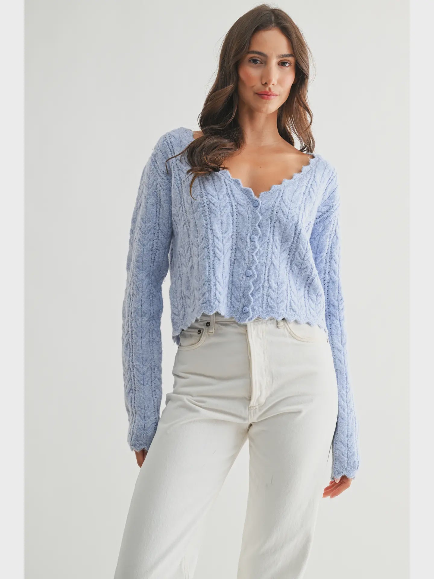 The Clara Cardigan in a soft pastel hue, featuring a cable-knit texture, scalloped hem and neckline, and button-front closure.

