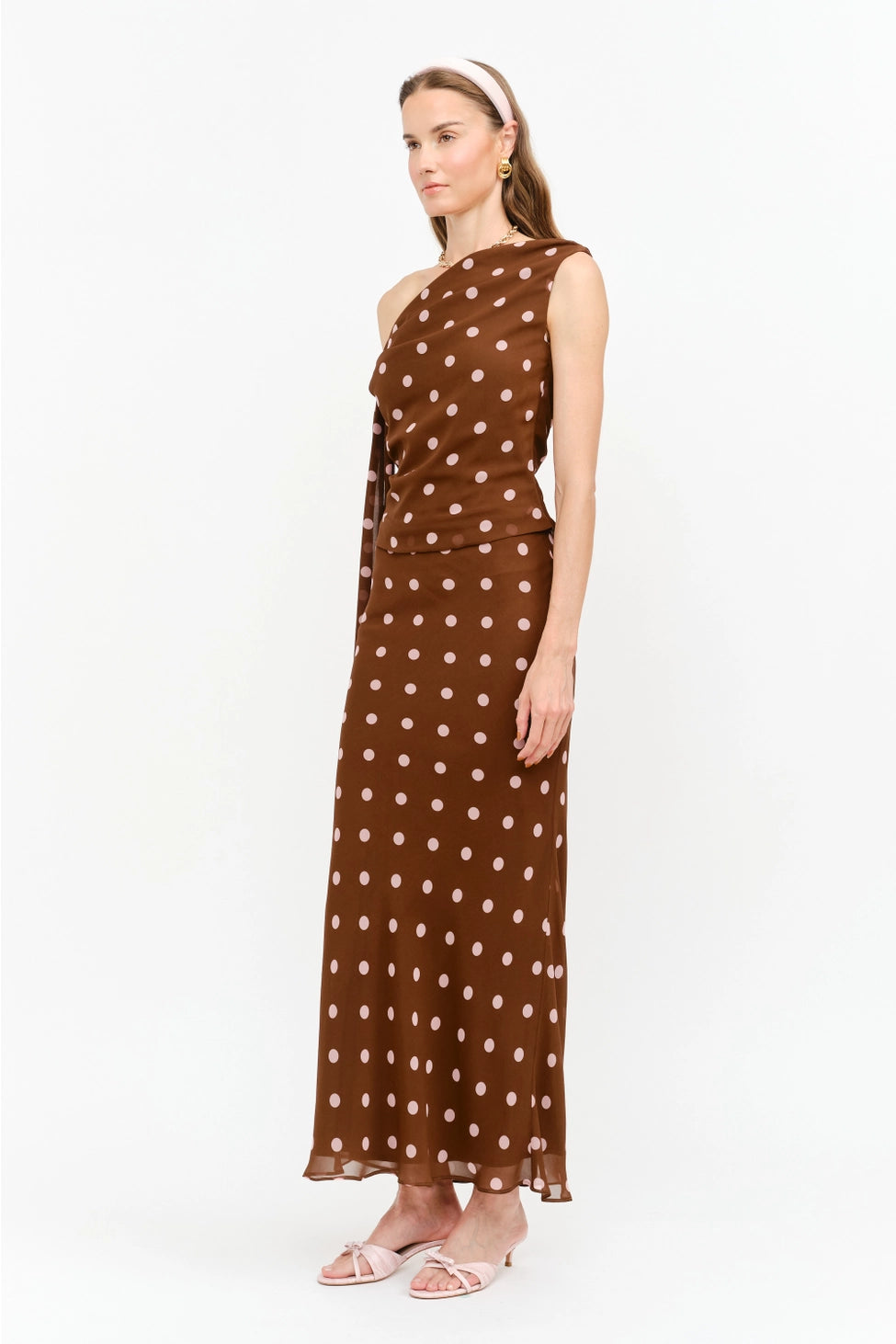 Celestine Off the Shoulder Top in brown featuring soft pink polka dots, an asymmetrical one-shoulder neckline, and a draped tie detail along the arm.