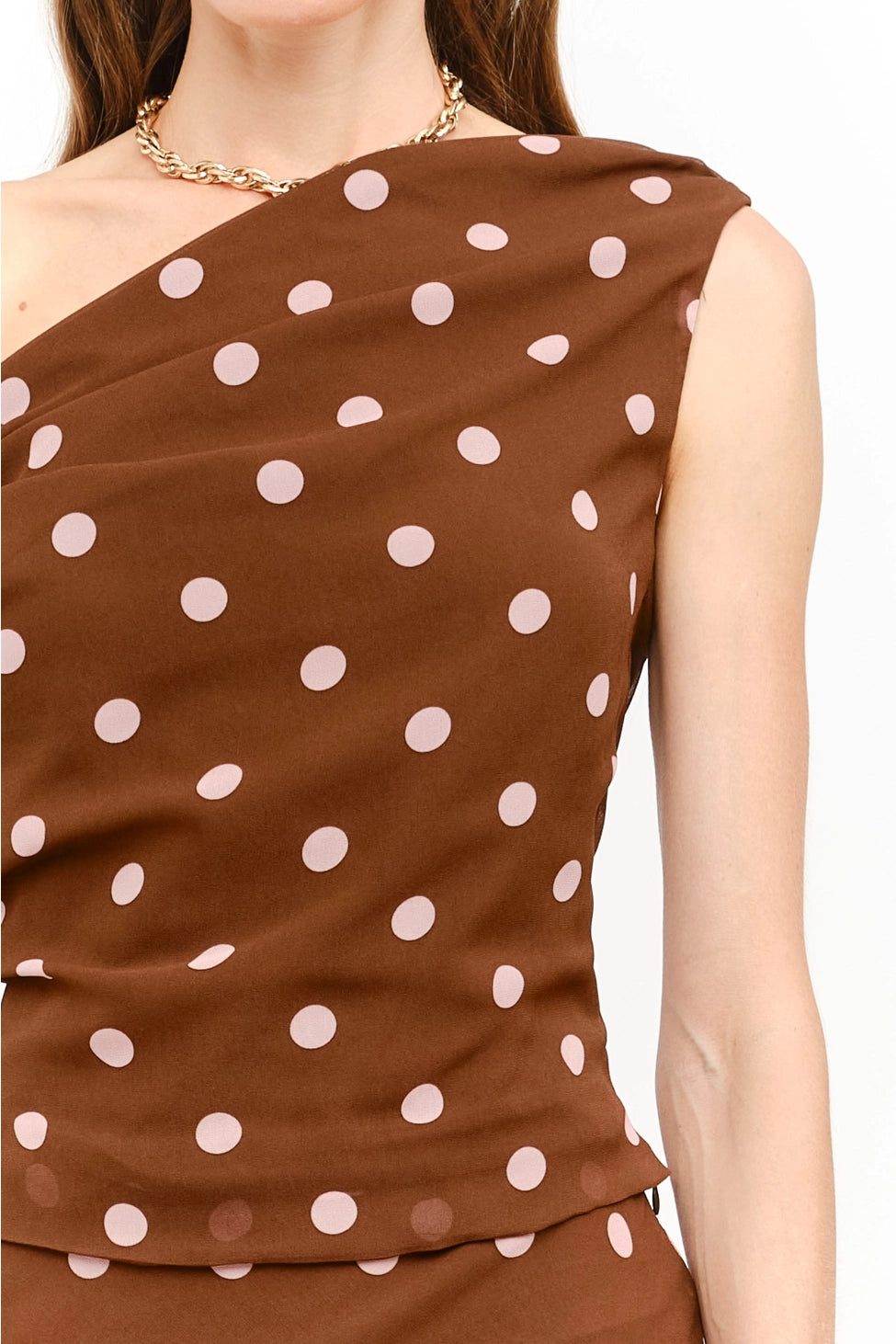 Celestine Off the Shoulder Top in brown featuring soft pink polka dots, an asymmetrical one-shoulder neckline, and a draped tie detail along the arm.