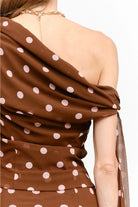 Celestine Off the Shoulder Top in brown featuring soft pink polka dots, an asymmetrical one-shoulder neckline, and a draped tie detail along the arm.