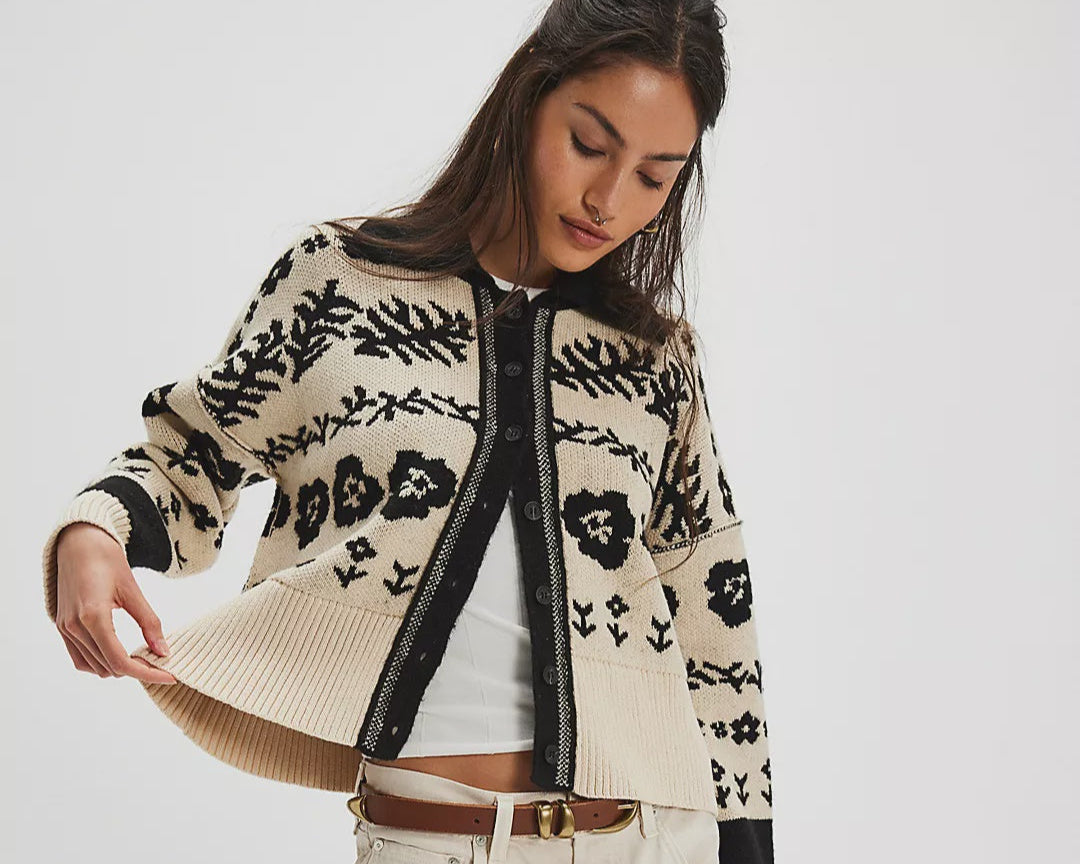 Woman wearing a patterned cardigan over a white shirt and beige shorts on a white background