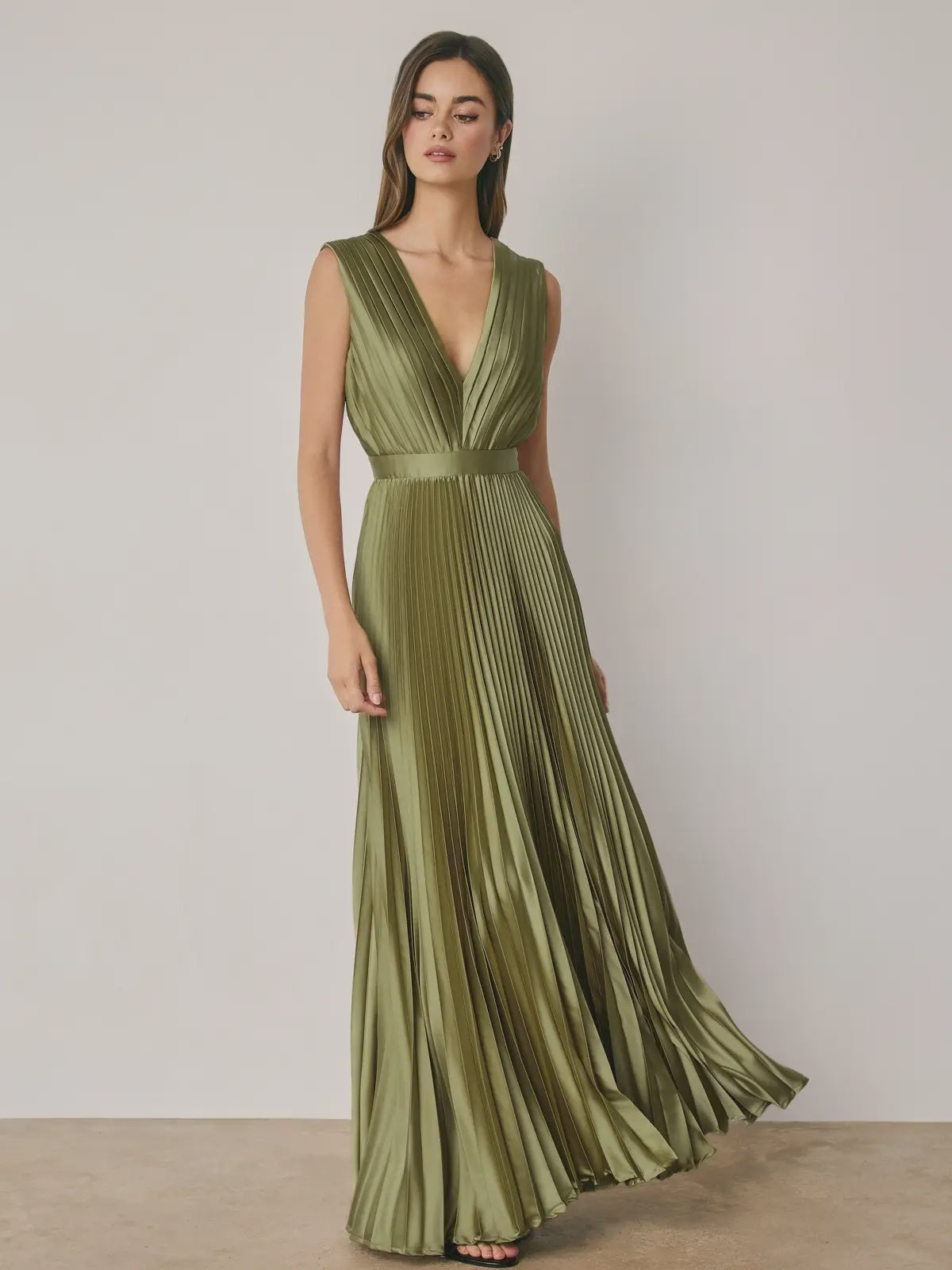 Alessia Pleated Satin Maxi Dress in Green featuring a flattering V-neckline, all-over accordion pleats, an empire waist with elastic waistband, and an adjustable tie-back detail. Designed with a flowing floor-length silhouette and a soft satin finish for an elegant, feminine look.