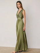 Alessia Pleated Satin Maxi Dress in Green featuring a flattering V-neckline, all-over accordion pleats, an empire waist with elastic waistband, and an adjustable tie-back detail. Designed with a flowing floor-length silhouette and a soft satin finish for an elegant, feminine look.