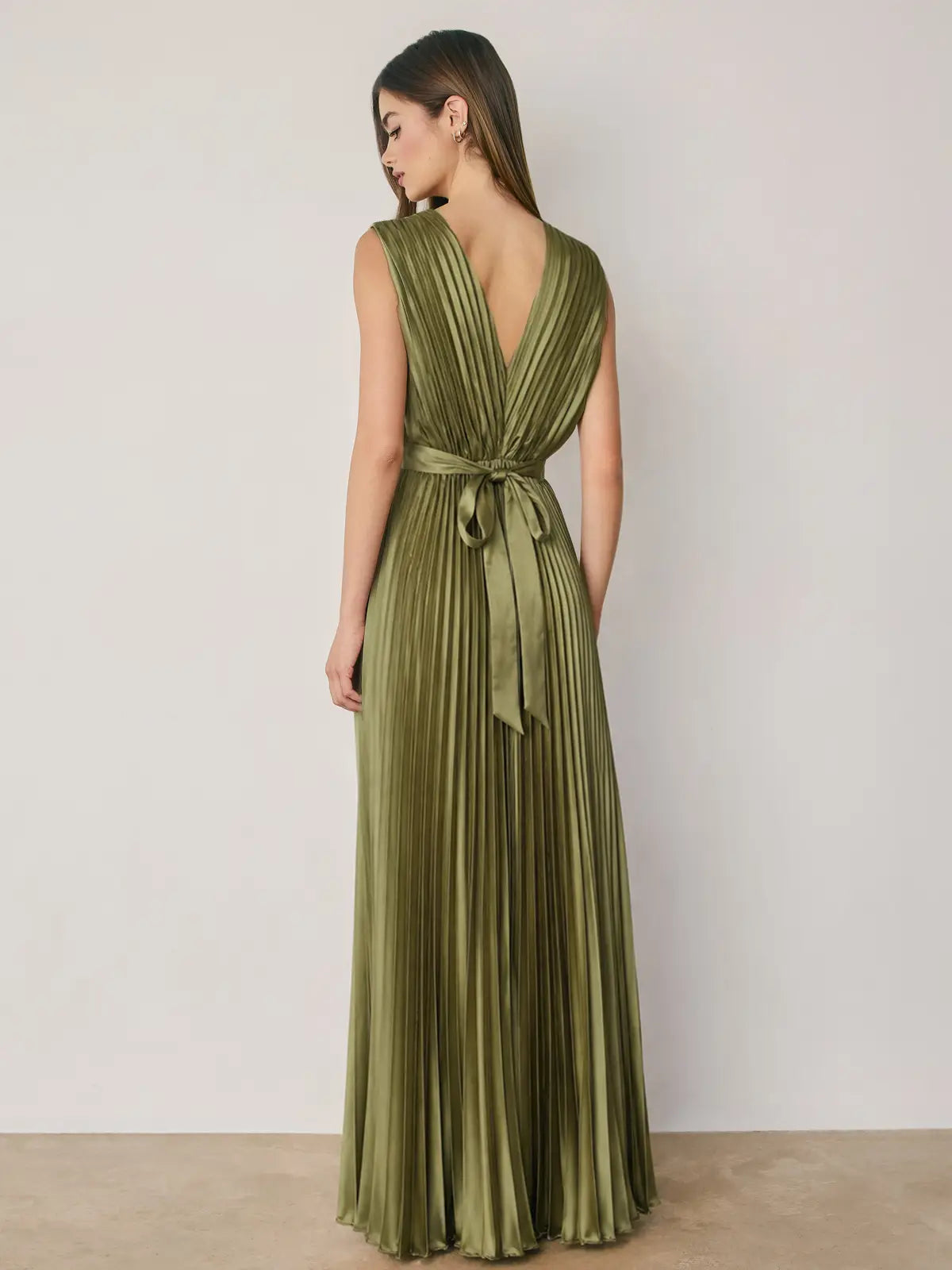 Alessia Pleated Satin Maxi Dress in Green featuring a flattering V-neckline, all-over accordion pleats, an empire waist with elastic waistband, and an adjustable tie-back detail. Designed with a flowing floor-length silhouette and a soft satin finish for an elegant, feminine look.