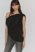 Cascadia Tunic in black featuring a draped off-the-shoulder neckline, soft slinky jersey fabric, ruched detailing, long sleeves, a relaxed longline silhouette, and an asymmetrical hem.