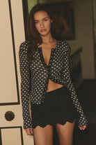 Fitted waffle-knit cardigan in a chocolate polka dot print with a crew neckline, long fitted sleeves, and snap-button front closure.