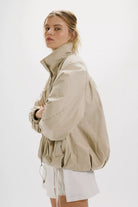 Free People Chelsea Funnel Neck Jacket in Oatmeal featuring an oversized slouchy fit, lightweight cotton-blend fabric, funnel-neck collar, raglan sleeves, adjustable drawcord waist, front zipper closure, and side slit pockets.