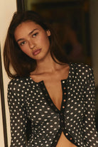 Fitted waffle-knit cardigan in a chocolate polka dot print with a crew neckline, long fitted sleeves, and snap-button front closure.