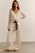 Textured lace cardigan in ivory, featuring a fitted longline silhouette, V-neckline, button-front closure, fitted long sleeves, and cascading ruffle hem detailing.