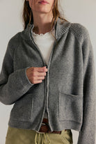 Women's ribbed knit zip-front sweater in cool grey with a high turtleneck collar, raglan sleeves, and front patch pockets.