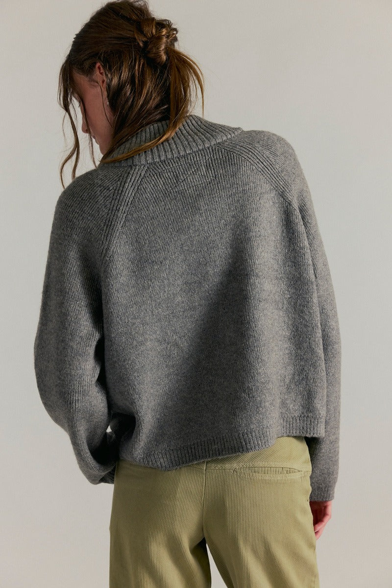 Women's ribbed knit zip-front sweater in cool grey with a high turtleneck collar, raglan sleeves, and front patch pockets.