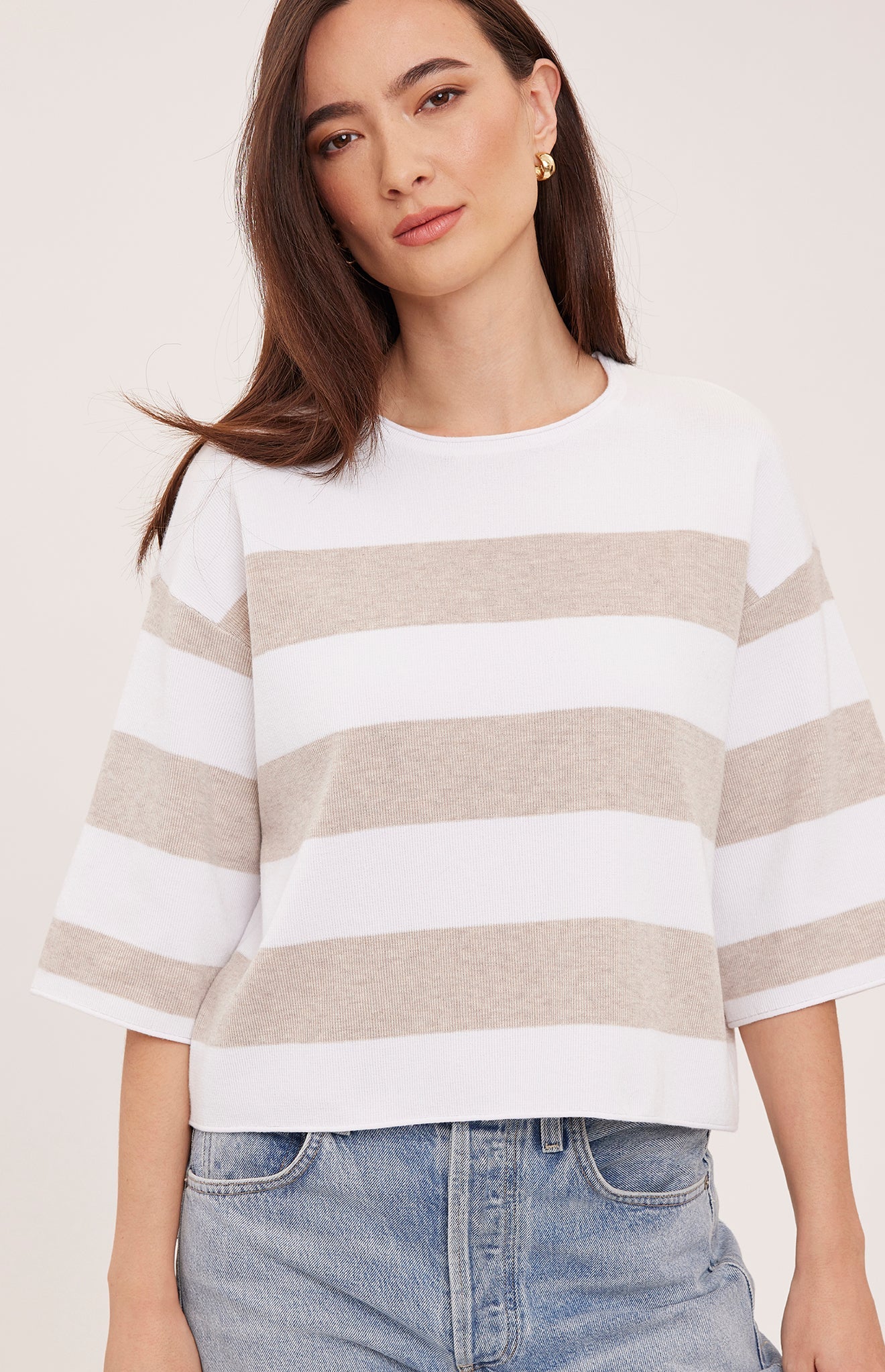 Woman wearing the Gentle Fawn Amina Knit Top in Heather Cream Stripe, featuring a relaxed fit, crew neckline, rolled hem details, and soft beige and cream horizontal stripes.