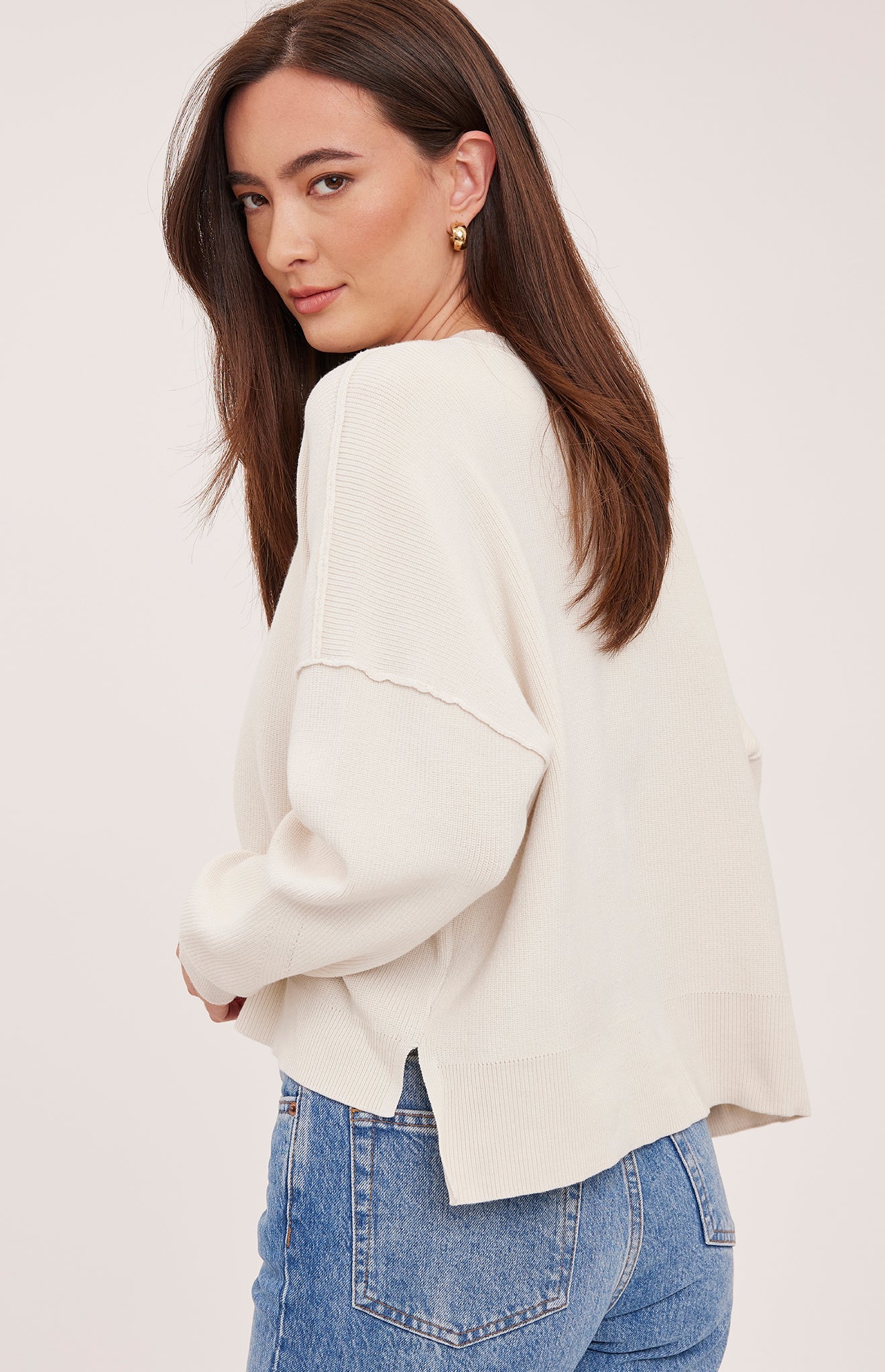 Women's cream oversized knit pullover sweater featuring a classic crew neckline, exposed seam detailing, side slits, and a soft textured half-cardigan stitch.