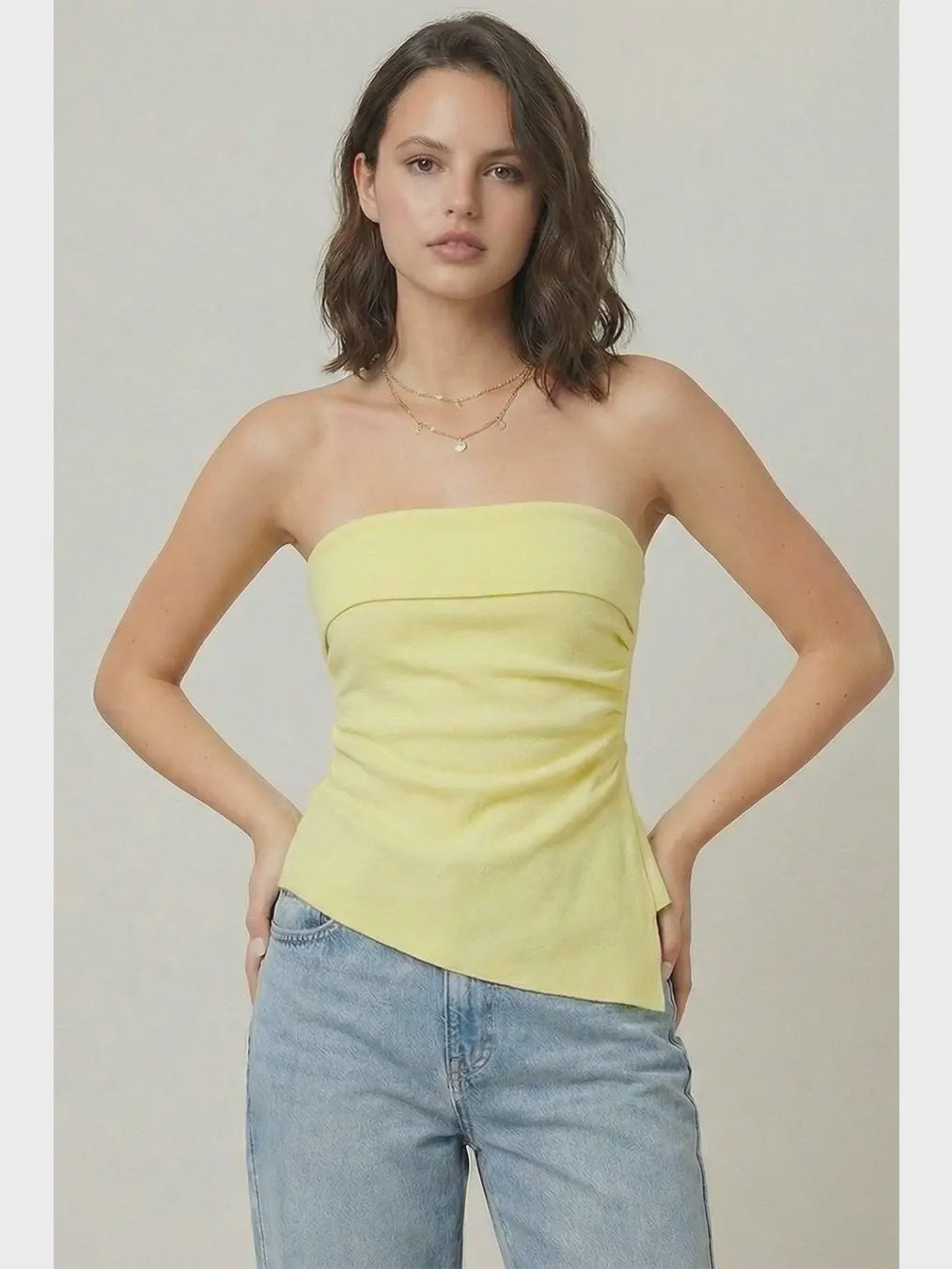 Woman wearing a strapless yellow top and blue jeans against a plain background