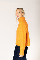 Amber yellow knit sweater featuring a mock neckline, relaxed fit, dropped shoulders, long sleeves, and ribbed cuffs and hem.
