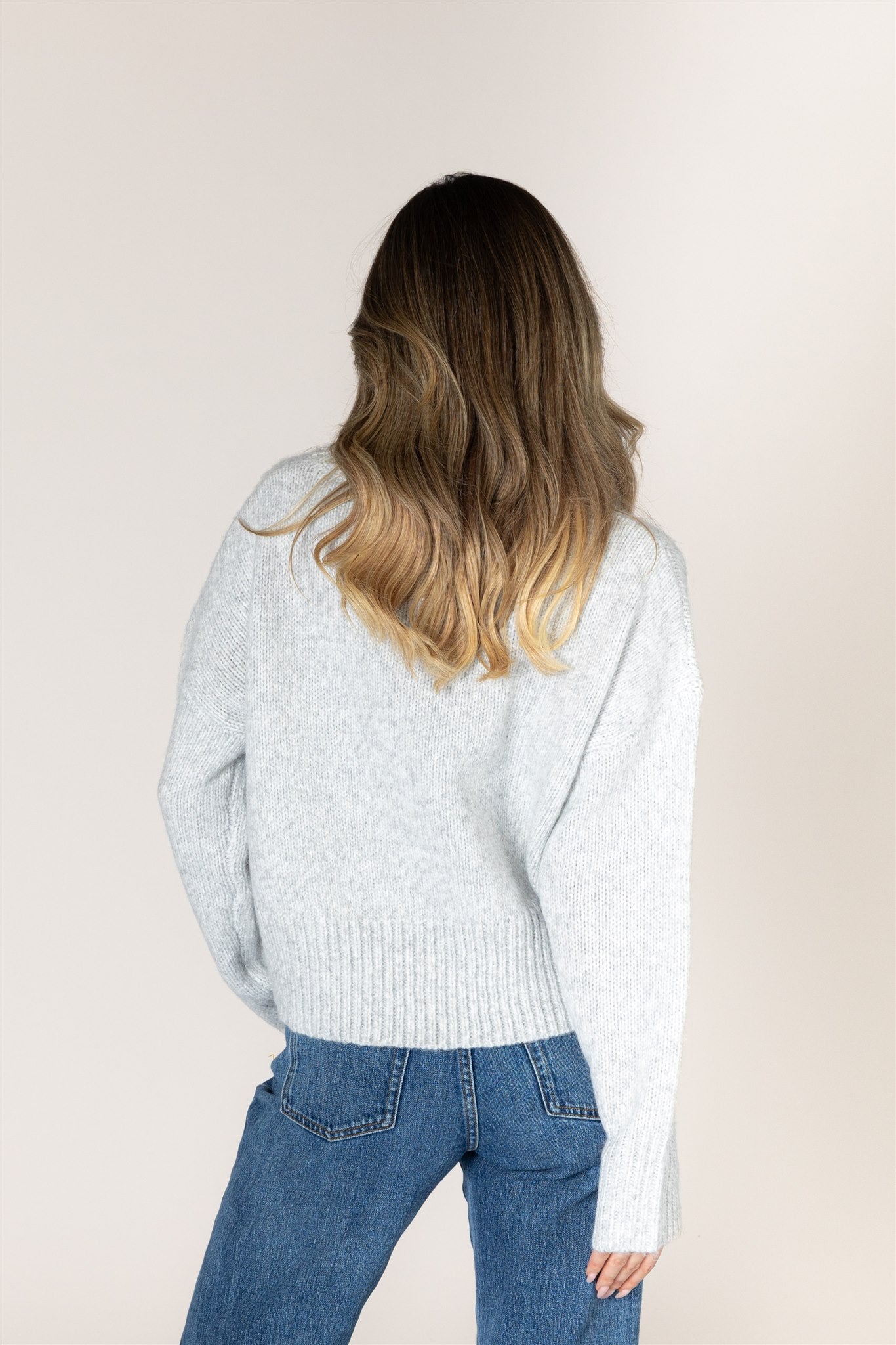 Light ash grey knit sweater featuring a mock neckline, relaxed fit, dropped shoulders, long sleeves, and ribbed cuffs and hem.