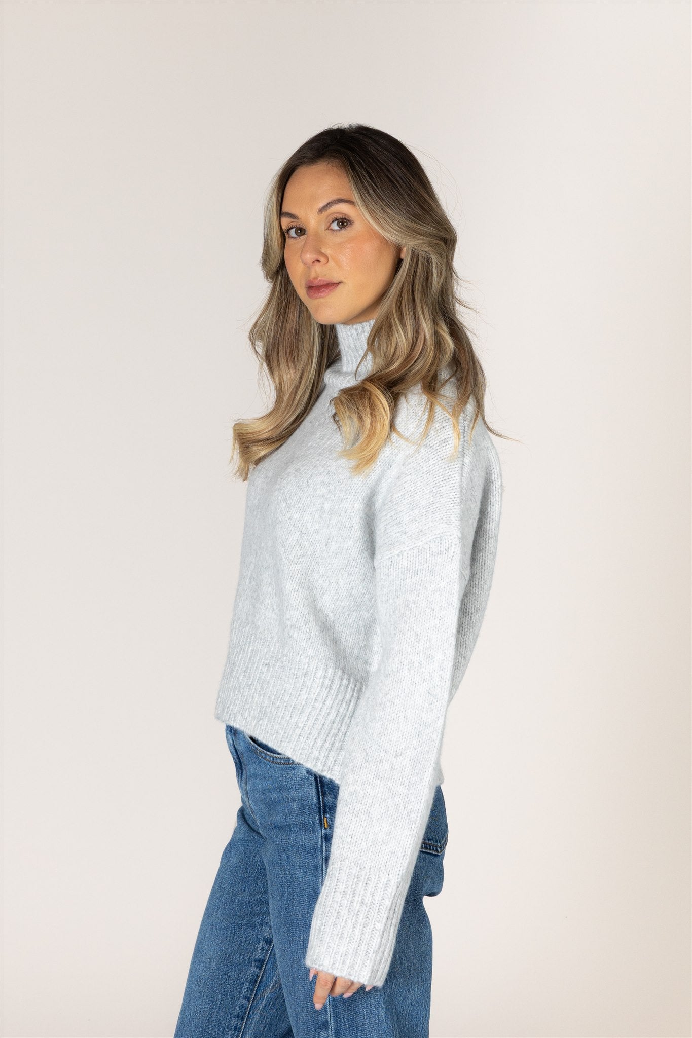 Light ash grey knit sweater featuring a mock neckline, relaxed fit, dropped shoulders, long sleeves, and ribbed cuffs and hem.