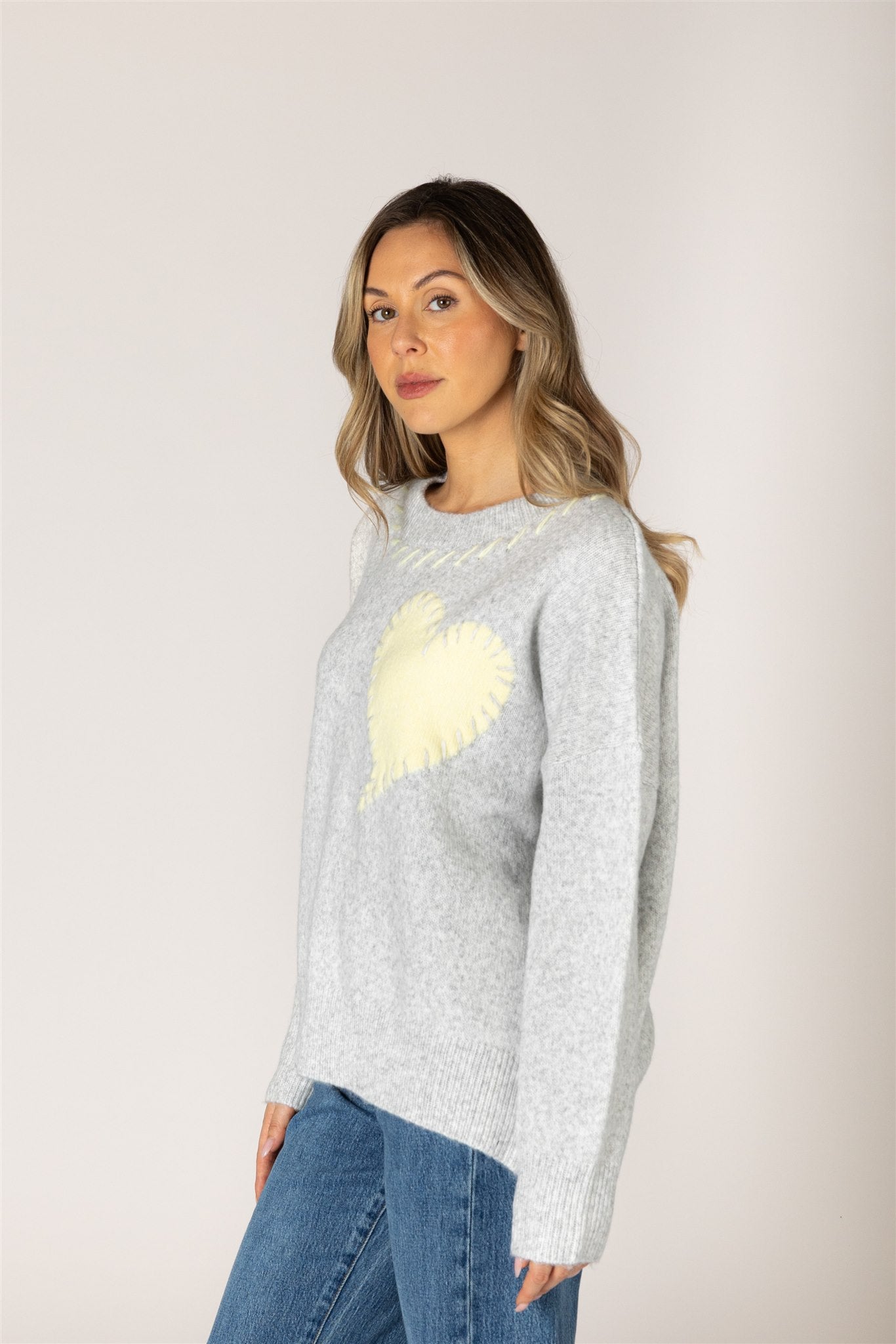 Ash grey crewneck sweater featuring a pale lemonade heart appliqué with contrast whipstitch detailing, long sleeves, and ribbed cuffs, hem, and neckline.