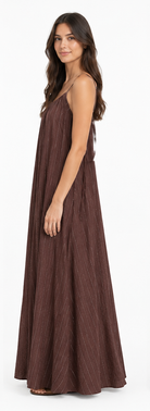 Model is wearing a chocolate-brown and white striped maxi dress with a relaxed, flowing floor-length silhouette and adjustable spaghetti straps.
