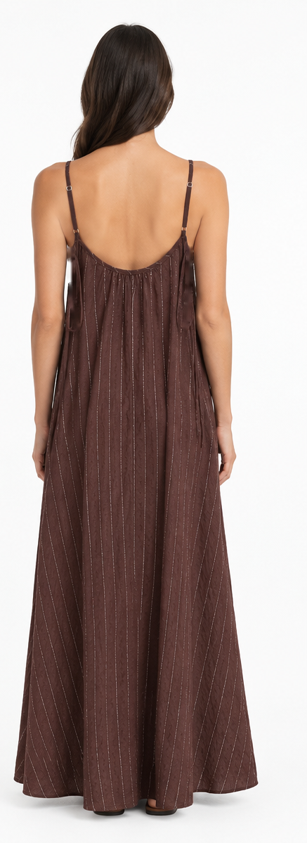 Model is wearing a chocolate-brown and white striped maxi dress with a relaxed, flowing floor-length silhouette and adjustable spaghetti straps.