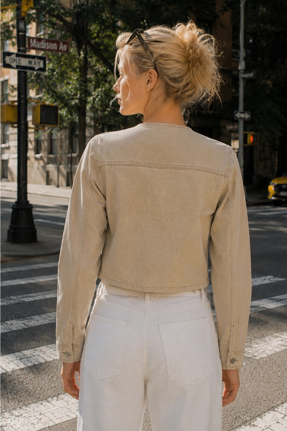 The Veda Cropped Utility Jacket in a soft sand denim wash, featuring a collarless neckline, flap chest pockets, structured seam detailing, and a cropped silhouette.
