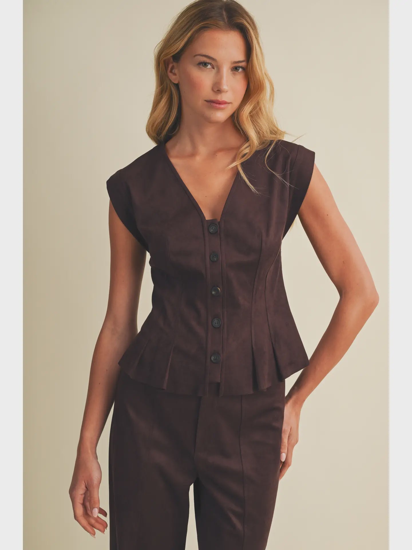 Faux suede sleeveless top with a V-neckline, button-front closure, extended shoulders, princess seams, and pleated peplum hem. Model is 5'9" and wearing a size Small.