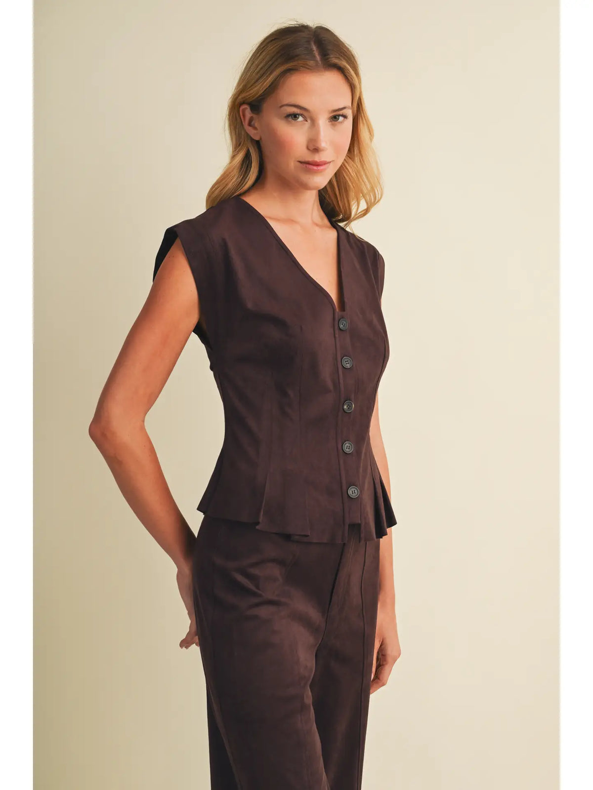 Faux suede sleeveless top with a V-neckline, button-front closure, extended shoulders, princess seams, and pleated peplum hem. Model is 5'9" and wearing a size Small.