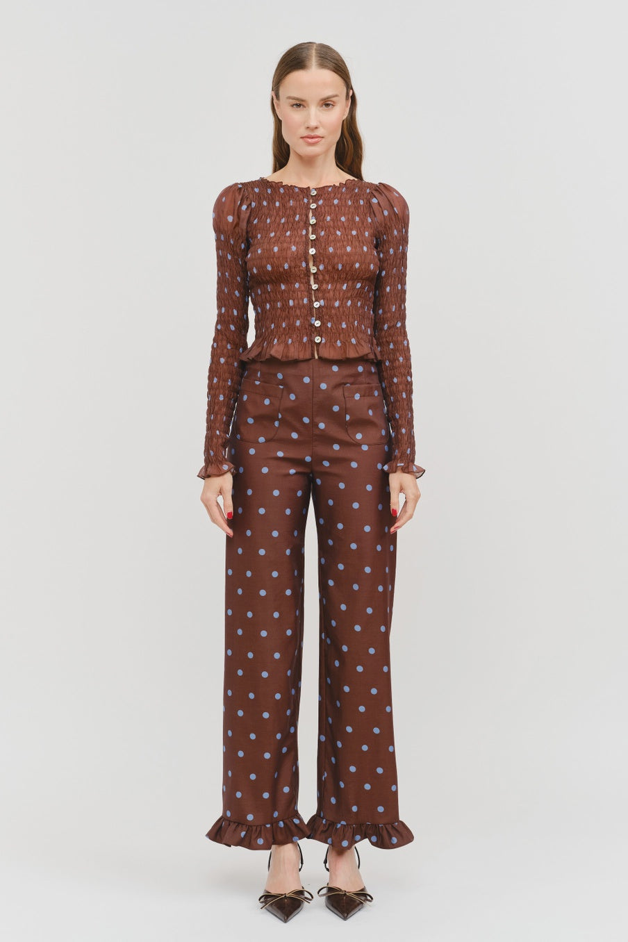 Women’s brown polka dot smocked long sleeve top featuring front buttons, puff sleeves, a fitted silhouette, and ruffled hem.