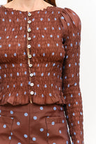 Women’s brown polka dot smocked long sleeve top featuring front buttons, puff sleeves, a fitted silhouette, and ruffled hem.