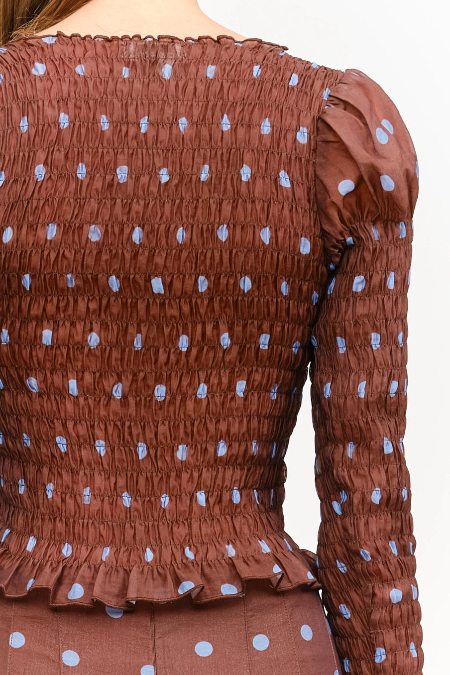 Women’s brown polka dot smocked long sleeve top featuring front buttons, puff sleeves, a fitted silhouette, and ruffled hem.