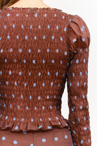 Women’s brown polka dot smocked long sleeve top featuring front buttons, puff sleeves, a fitted silhouette, and ruffled hem.