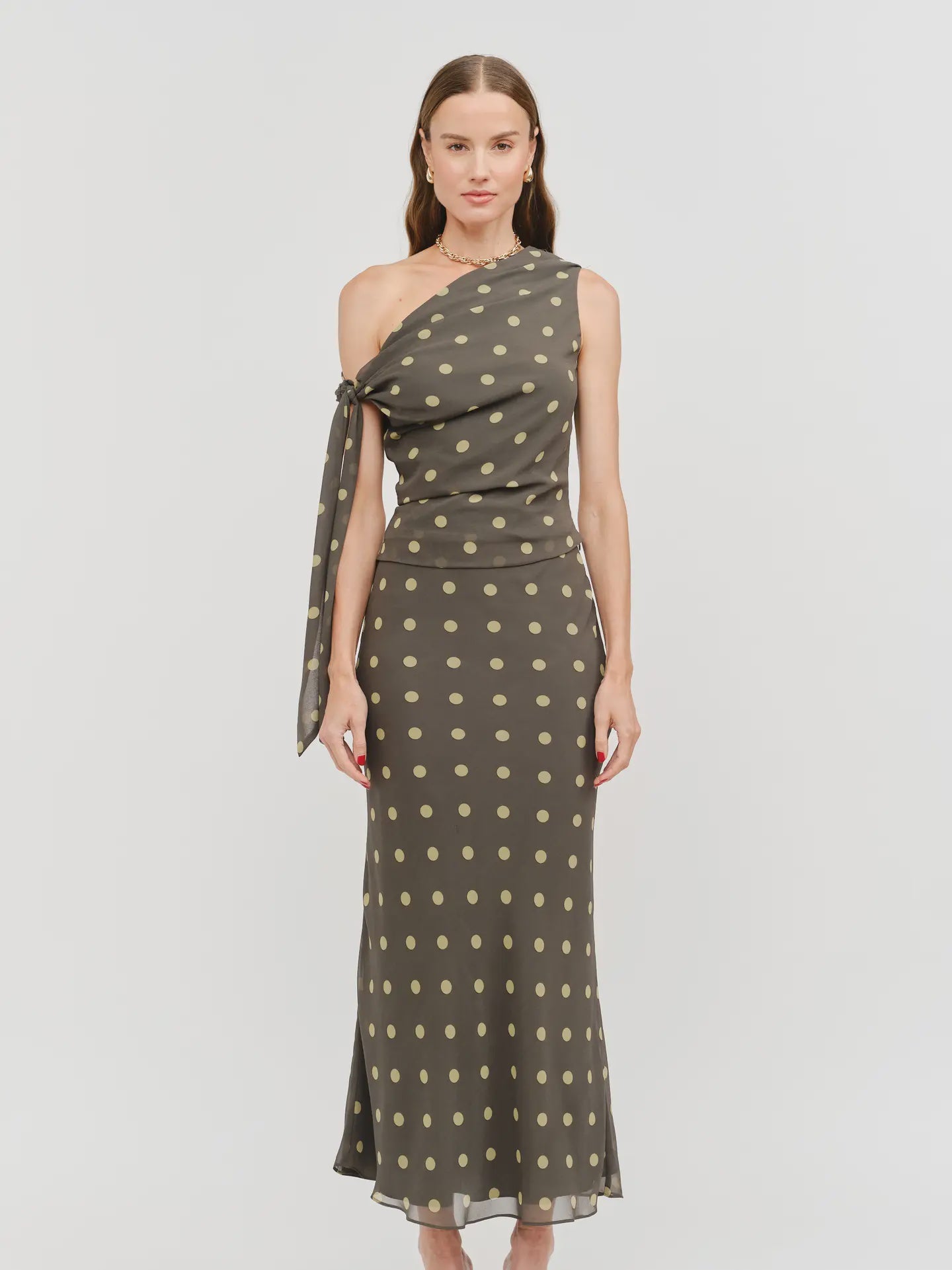 Celestine Off The Shoulder Top featuring a lightweight chiffon fabric with a contrasting polka dot print, asymmetrical one-shoulder neckline, soft draped detailing, and an elegant side tie. Designed with a flattering, feminine silhouette and a slightly relaxed fit.