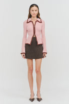 Model wearing the Jacquie Knit Top in light pink, featuring a fitted silhouette, long sleeves, collared neckline, contrasting burgundy fuzzy trim, and two-way front zipper closure.