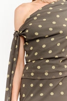 Celestine Off The Shoulder Top featuring a lightweight chiffon fabric with a contrasting polka dot print, asymmetrical one-shoulder neckline, soft draped detailing, and an elegant side tie. Designed with a flattering, feminine silhouette and a slightly relaxed fit.