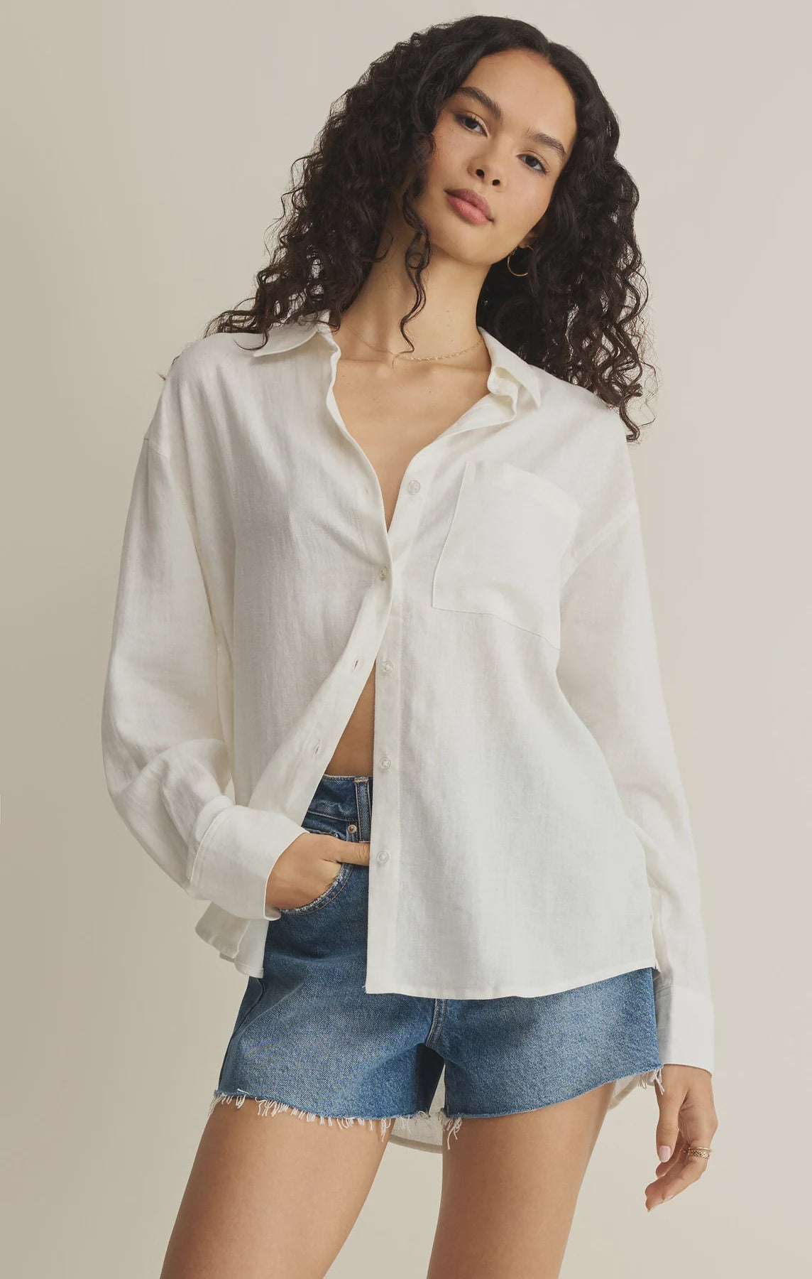 Woman wearing a white button-up shirt and denim shorts on a beige background