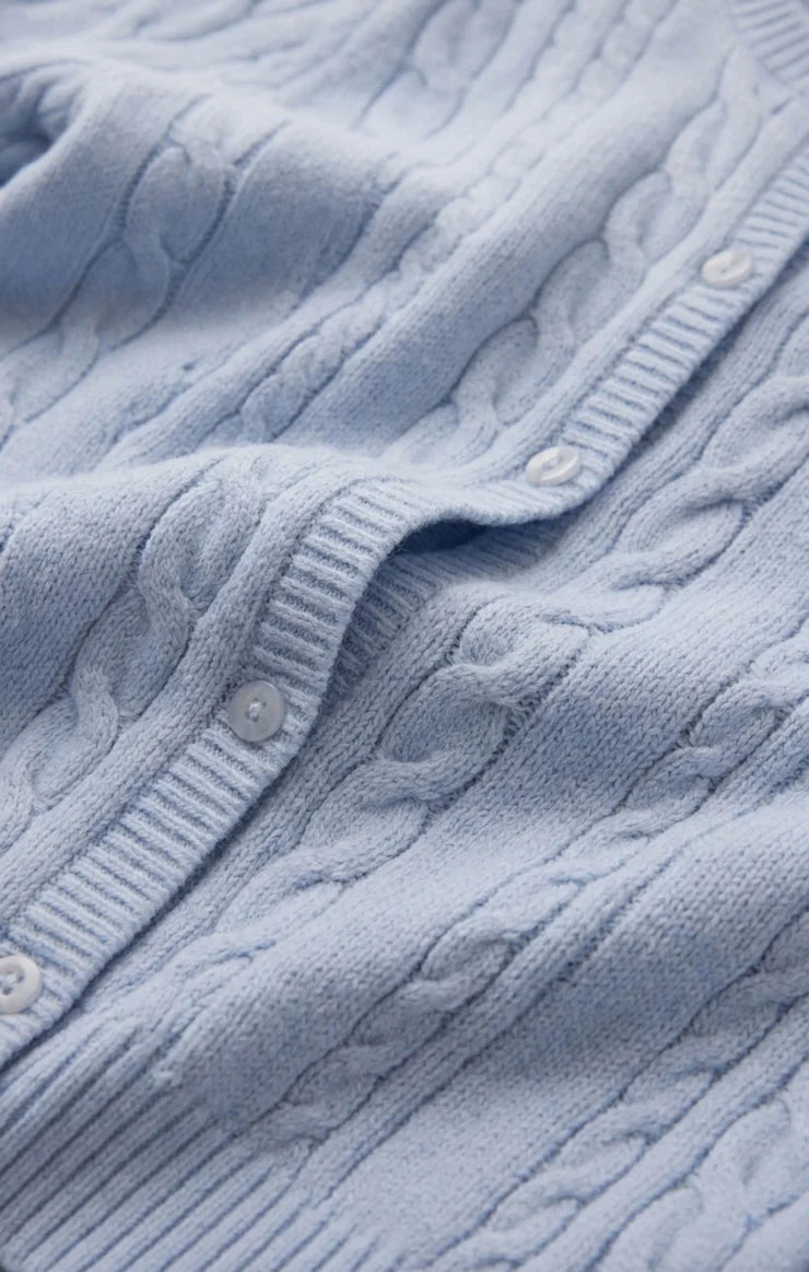 Close-up of a cable knit cardigan highlighting the textured knit pattern, crew neckline, button-front closure, and soft fabric. The detailed stitching and elevated finish showcase its classic, everyday design.