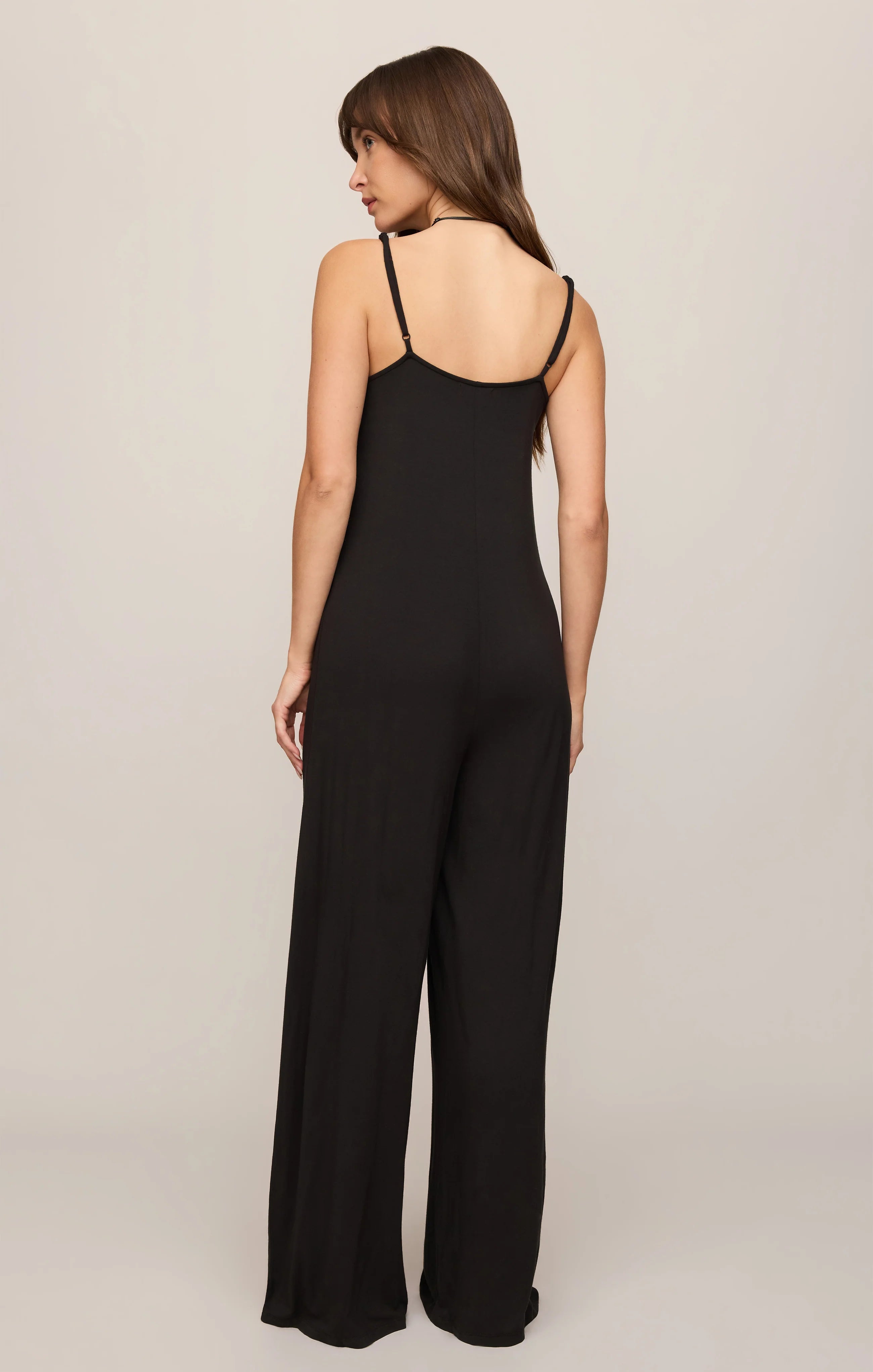 Model wearing the Z Supply Leyla Jumpsuit in black. The sleeveless jumpsuit features thin adjustable spaghetti straps, a V-neckline, a relaxed bodice with subtle seam detailing, and wide-leg pants that drape to the floor. 